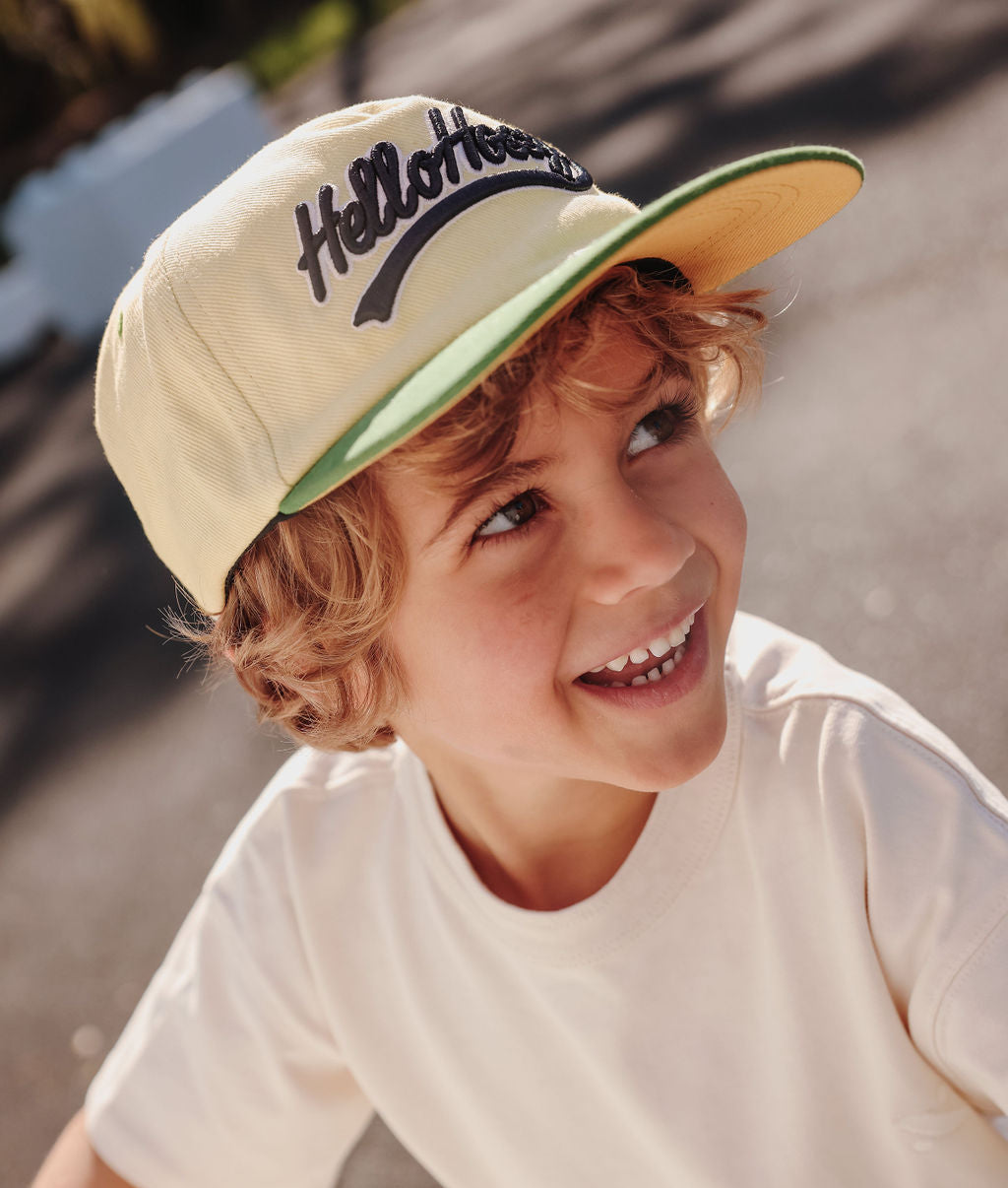 Bambino che indossa un cappellino bianco con visiera verde e ricamo Hello Hossy