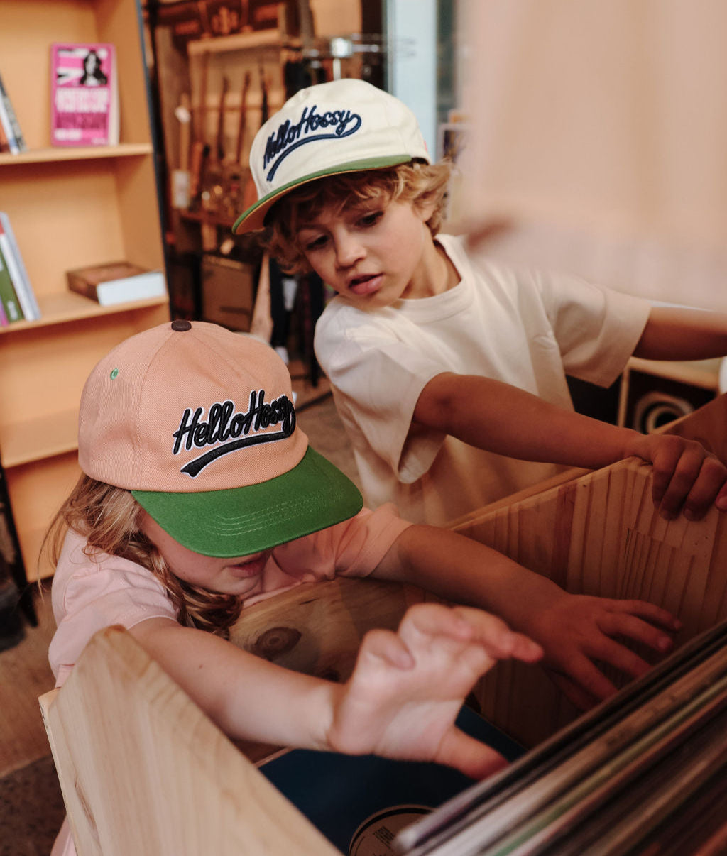 Bambino che indossa un cappellino marrone visiera verde ricamo Hello Hossy e bambino con cappellino beige Hello Hossy