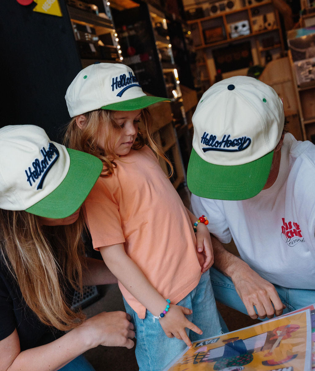 Bambino che indossa un cappellino bianco con visiera verde e ricamo Hello Hossy