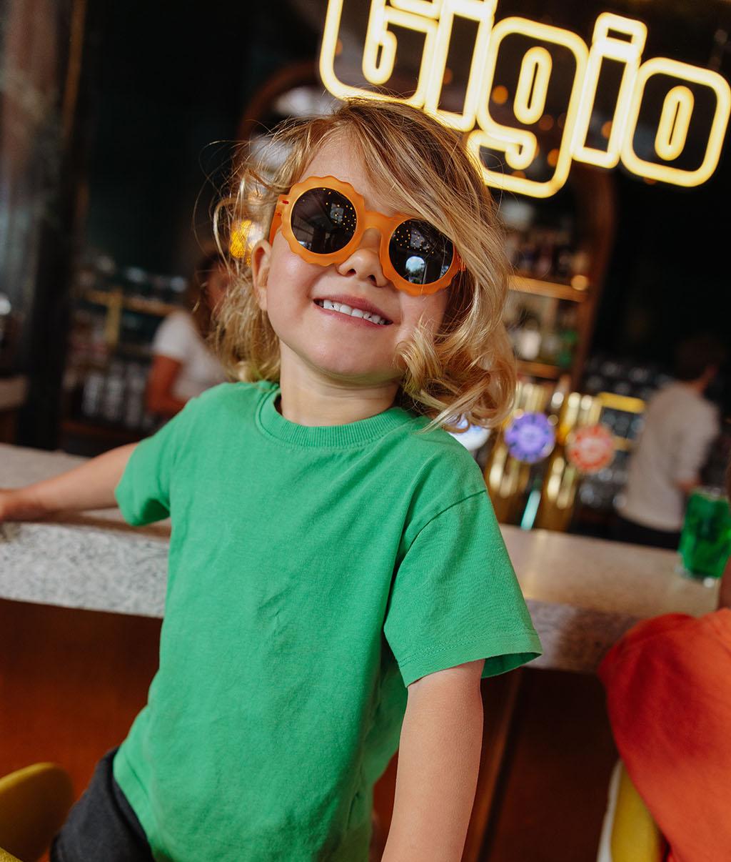 Occhiali da sole da bambino con montatura arancione, forma a fiore e lenti scure Hello Hossy