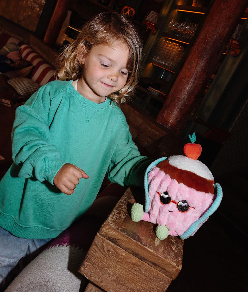 Bambina in piedi che tiene il peluche originale Cherry Cake appoggiato su una ringhiera - vista frontale - Hello Hossy