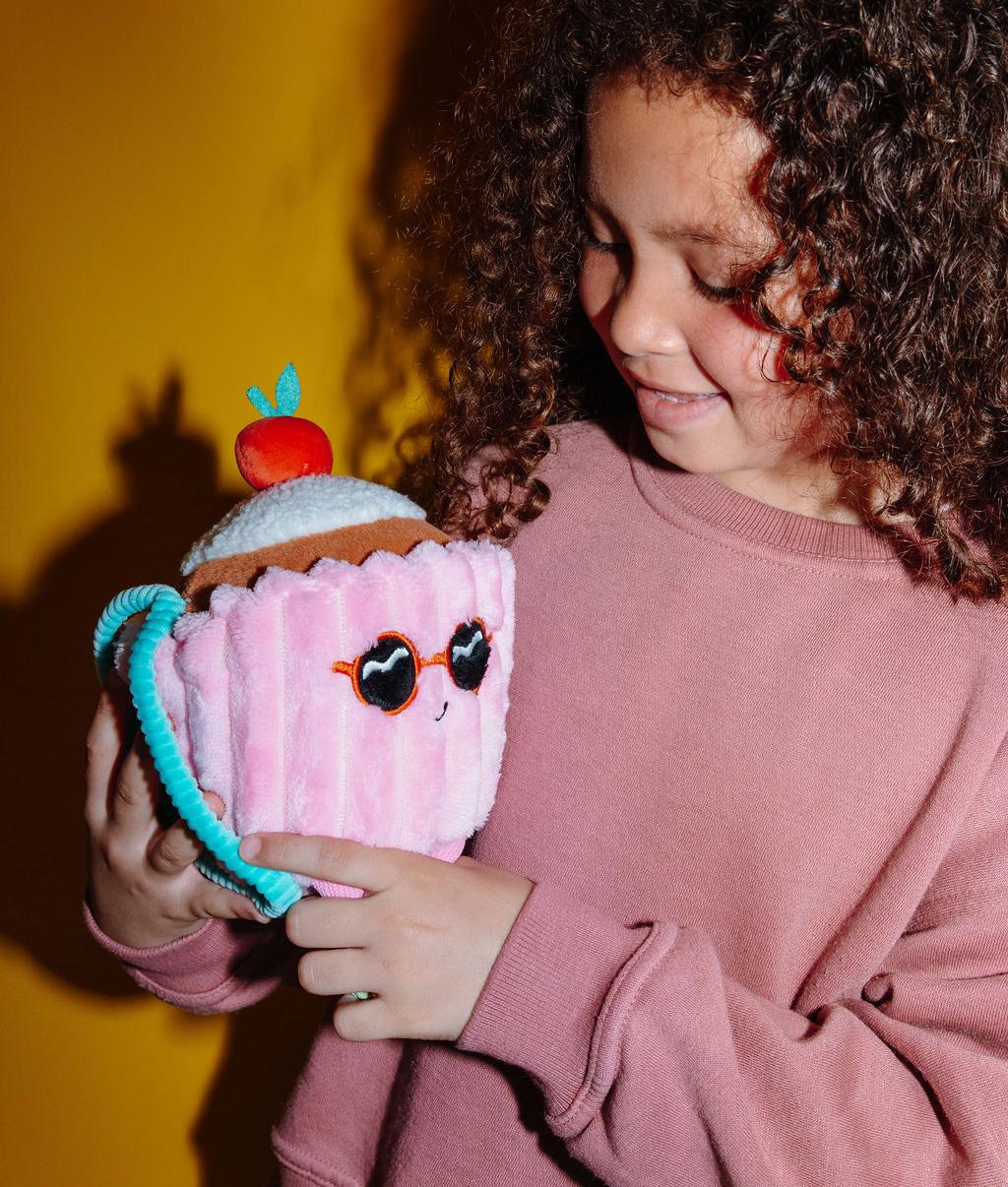 Peluche morbida a forma di torta con una ciliegia sopra, Cherry Cake, tenuta da un bambino – vista a 3/4 – Hello Hossy