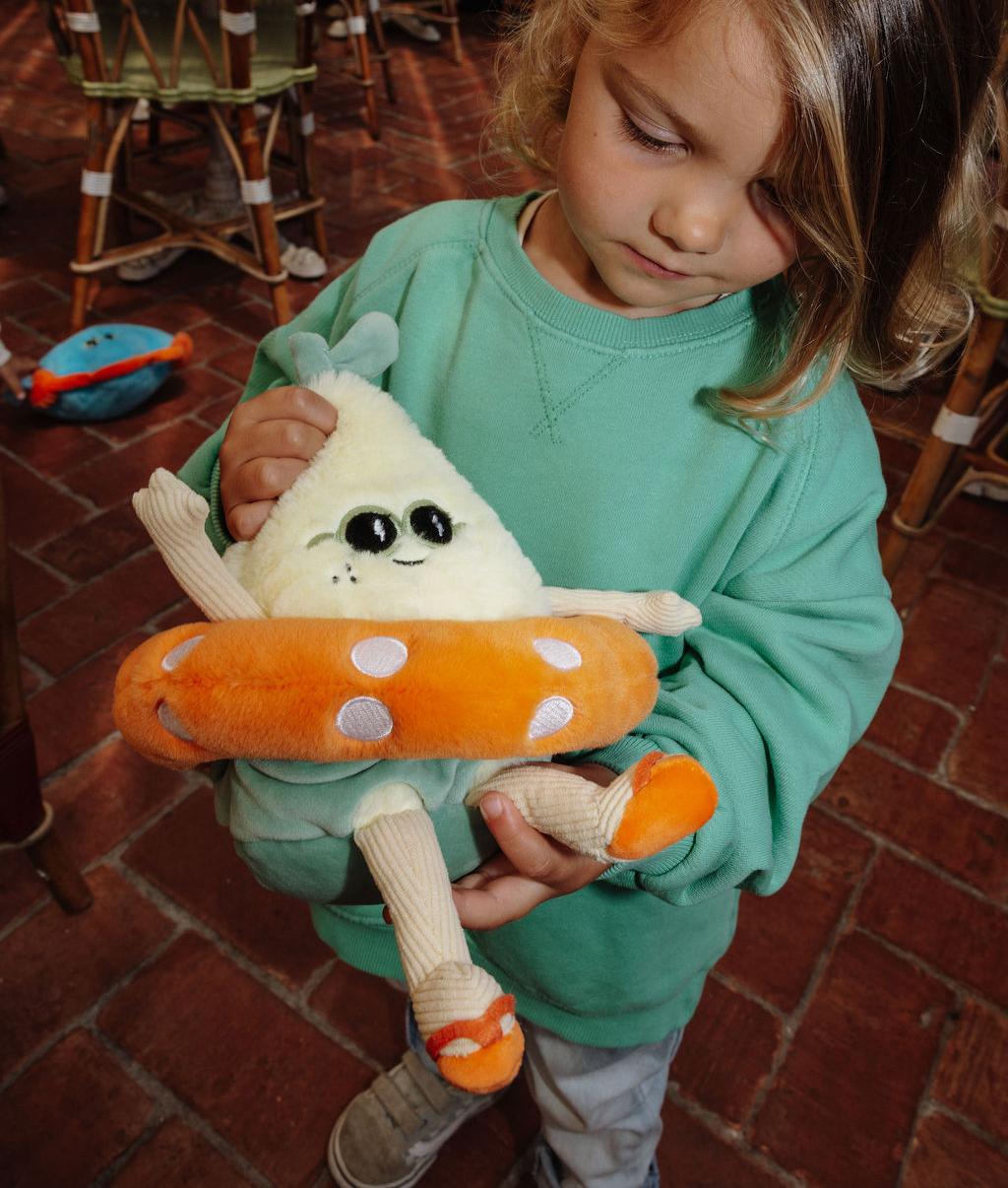 Bambina che tiene tra le mani la Peluche Lemon Splash a forma di limone con occhiali da sole e salvagente arancione - vista frontale - Hello Hossy