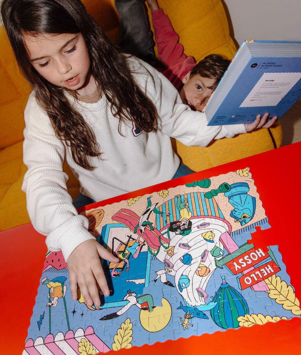 Bambina con il puzzle "Ice Cream Day" assemblato su un tavolo davanti a lei e con la scatola effetto libro in mano – foto lifestyle – Hello Hossy