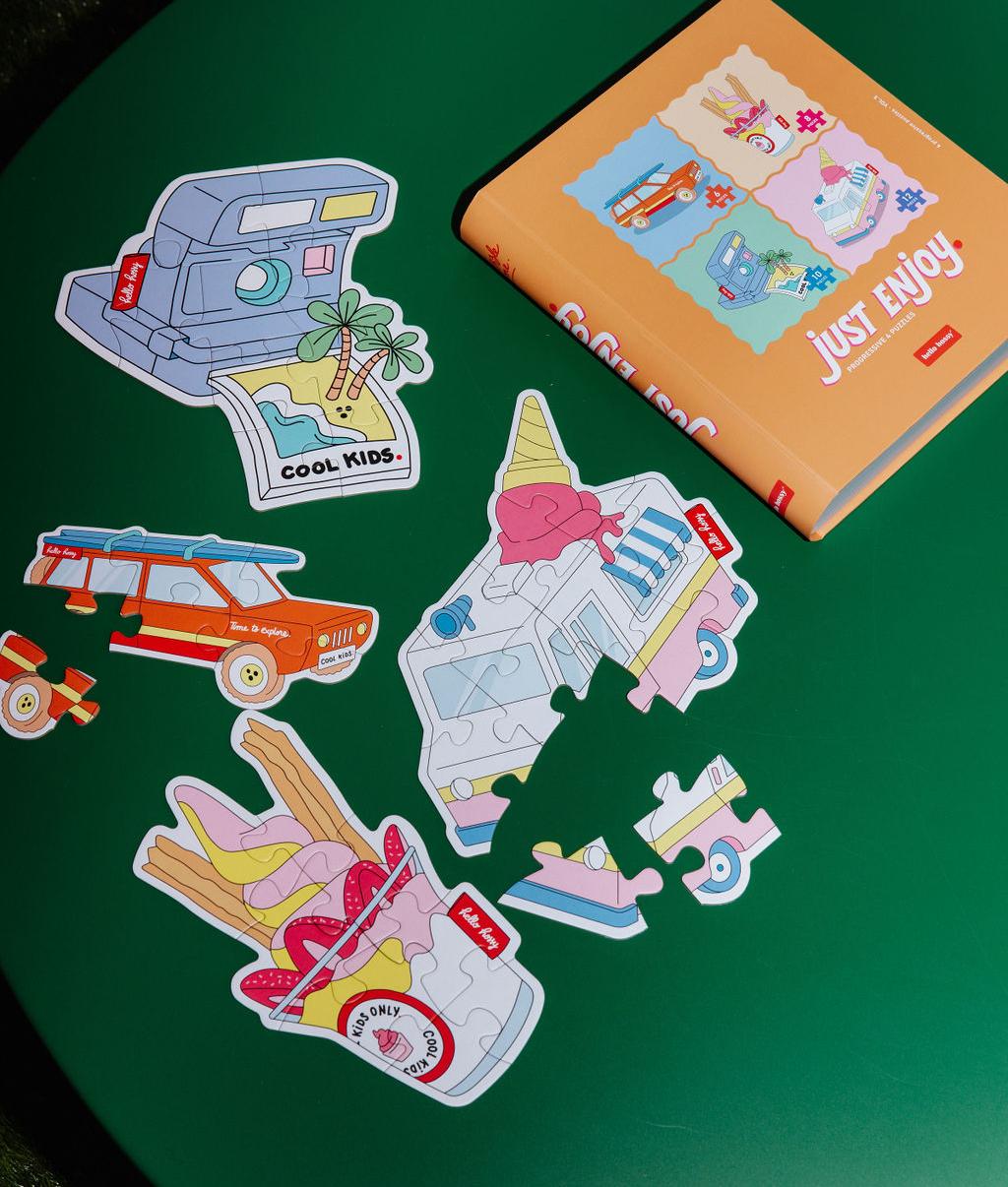Puzzle colorati "Just Enjoy" parzialmente assemblati su un tavolo, con la scatola accanto - vista dall'alto - Hello Hossy