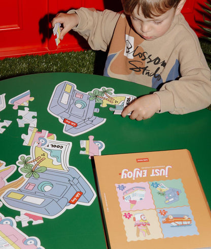 Bambino che assembla uno dei quattro puzzle a forma di macchina fotografica, su un tavolo - foto lifestyle - Hello Hossy