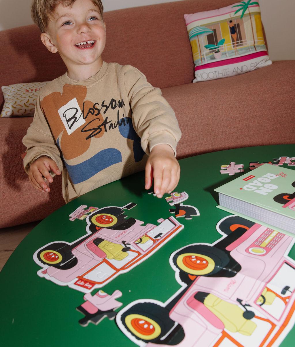 Bambino che compone il Puzzle colorato da 24 pezzi "On The Road" su un tavolo – atmosfera giocosa – Hello Hossy