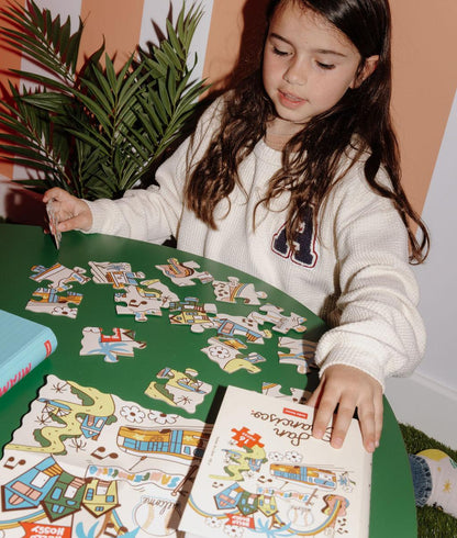 Bambina che compone il puzzle colorato da 16 pezzi "San Francisco" su un tavolo – vista frontale – Hello Hossy